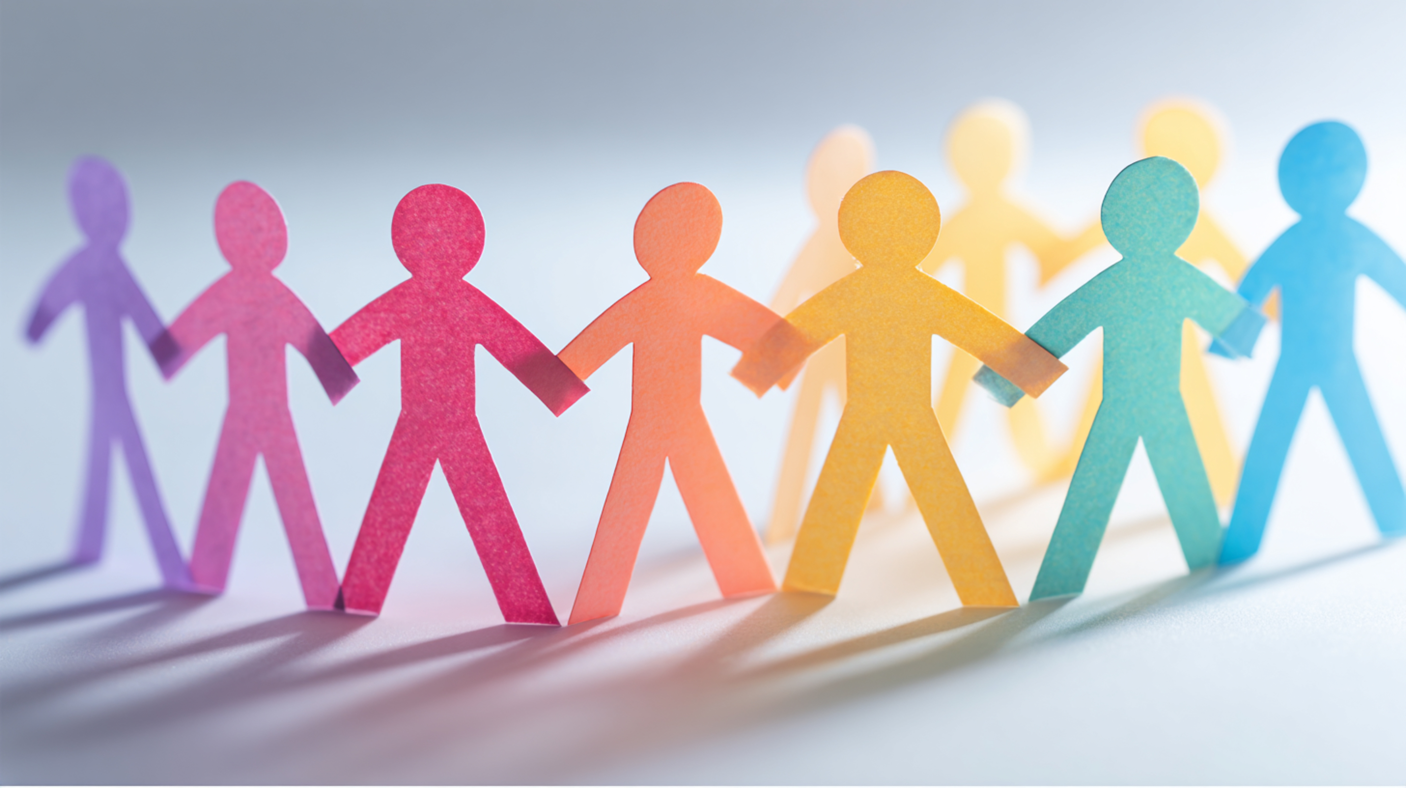 A group of human-shaped paper cut-outs in different colors holding hands, symbolizing unity and connection.