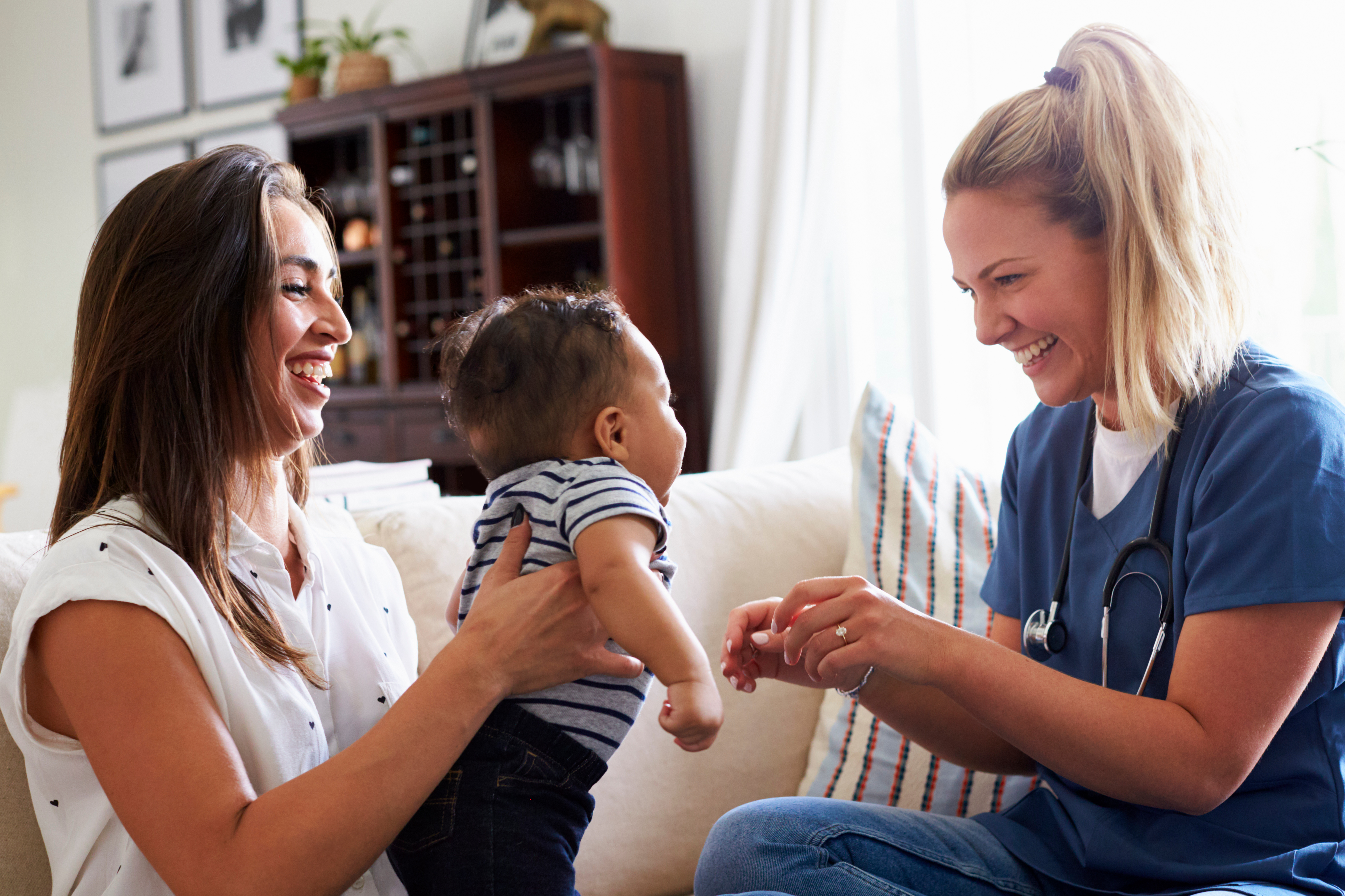 A mom, a baby, and a nurse sitting on a couch in a living room